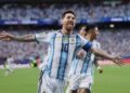 Argentine captain Lionel Messi, with his arms outstretched and sticking out his tongue in a spirited celebration, wearing the traditional white and light blue No. 10 shirt, after scoring for his country. A blurry teammate (number 16) is behind him, against a backdrop of a packed stadium crowd.